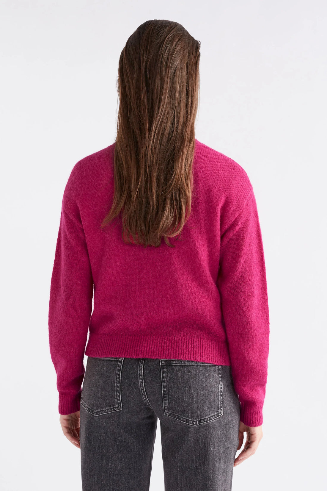 Woman facing the back wearing white top with Daru Cardigan in Bright pink and black denim pants