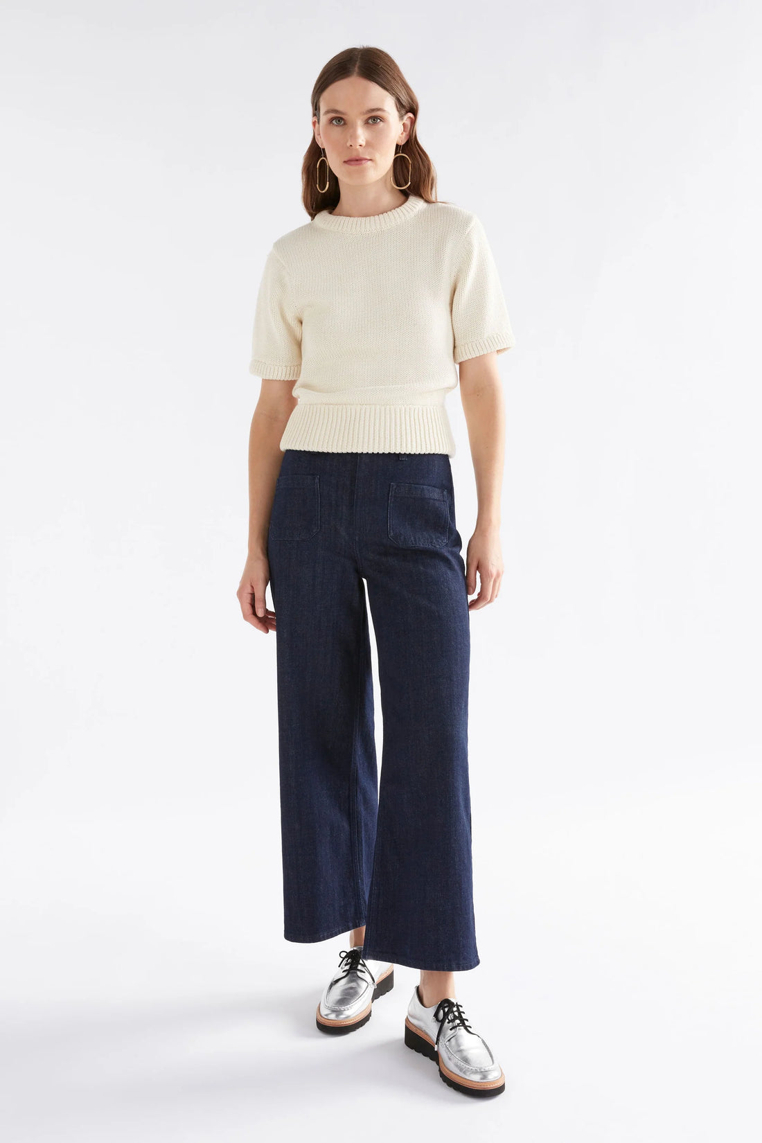 Woman wearing Luft Knit Top in white, denim pants, and silver shoes