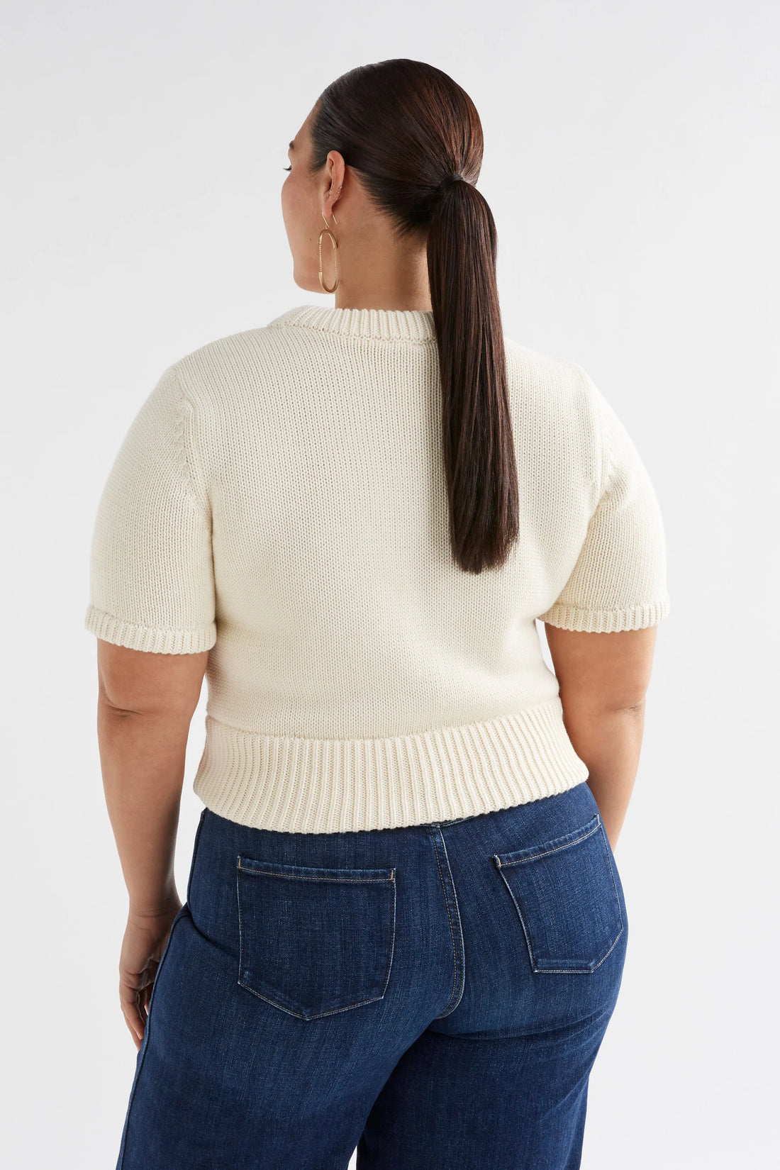 Plus size Woman wearing Luft Knit Top in white and denim pants facing the back