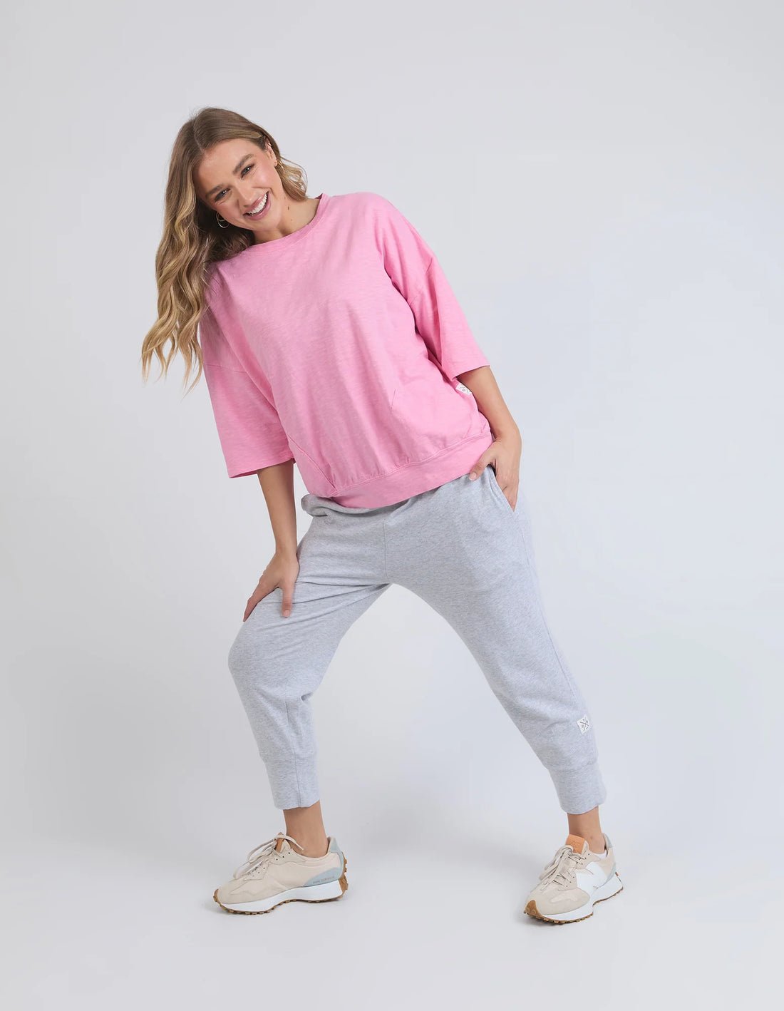 woman wearing elm lifestyle mazie sweat in strawberry pink, grey pants, and rubber shoes
