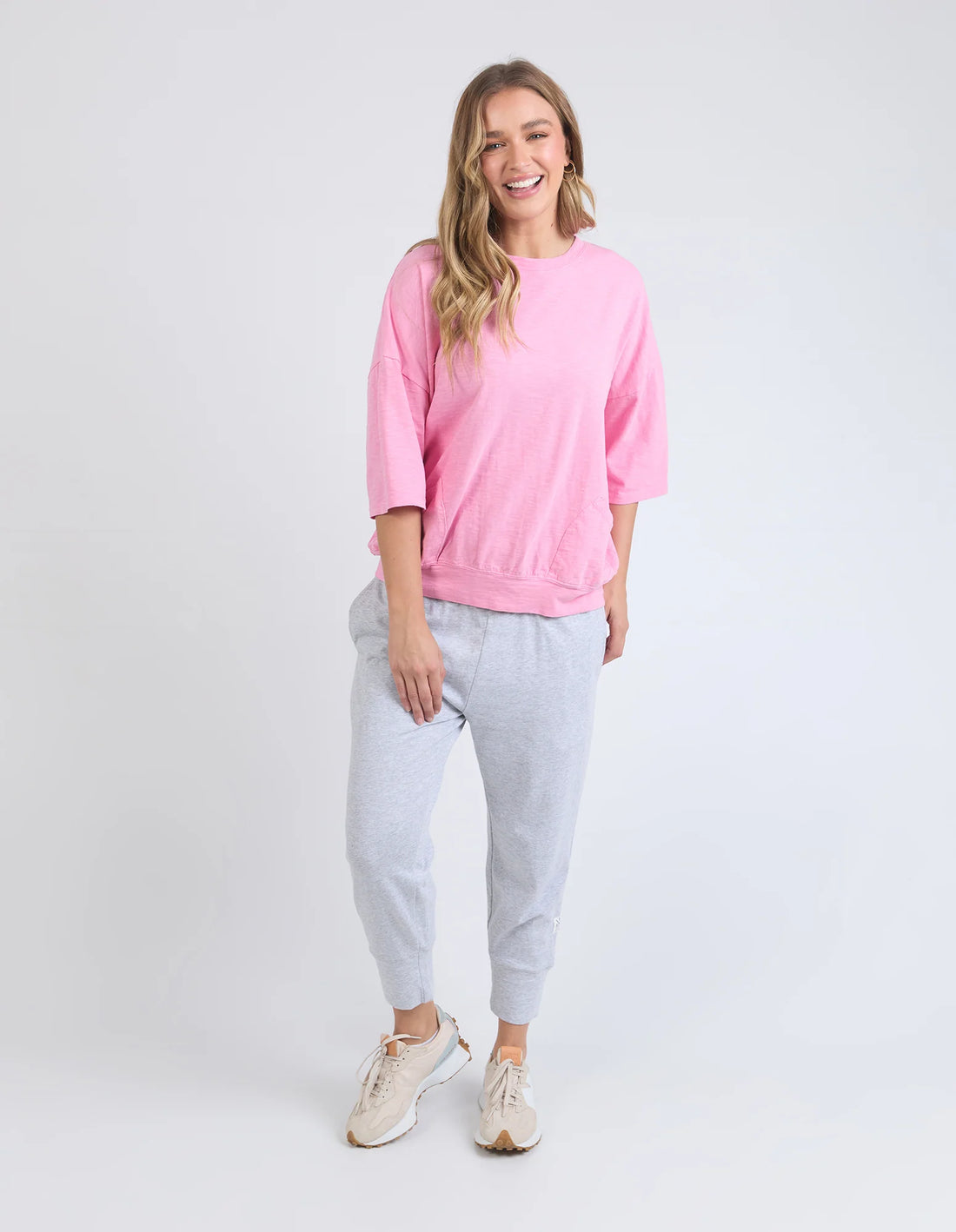 Woman wearing elm lifestyle mazie sweat in strawberry pink, grey pants, and rubber shoes
