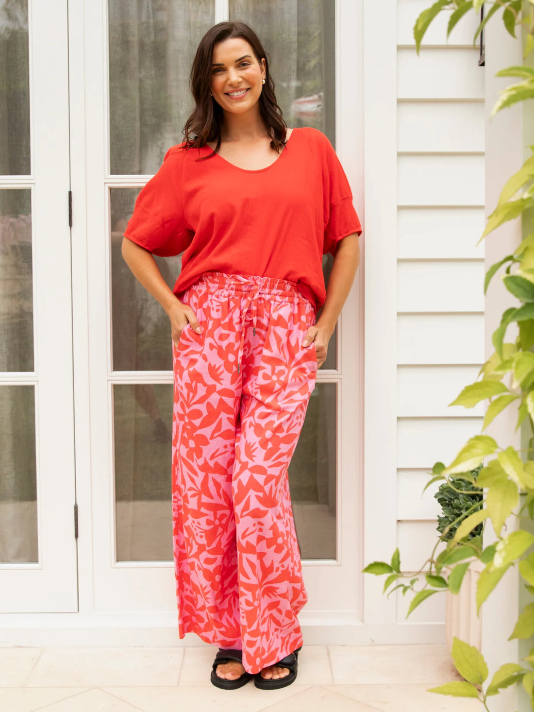 woman wearing elm lifestyle sunset hour print pant, red blouse and black slippers