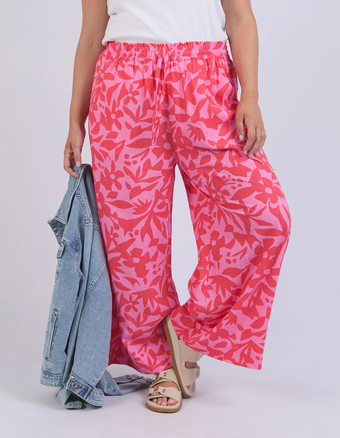 hand holding denim jacket, wearing white top, and sunset hour print pant, slippers
