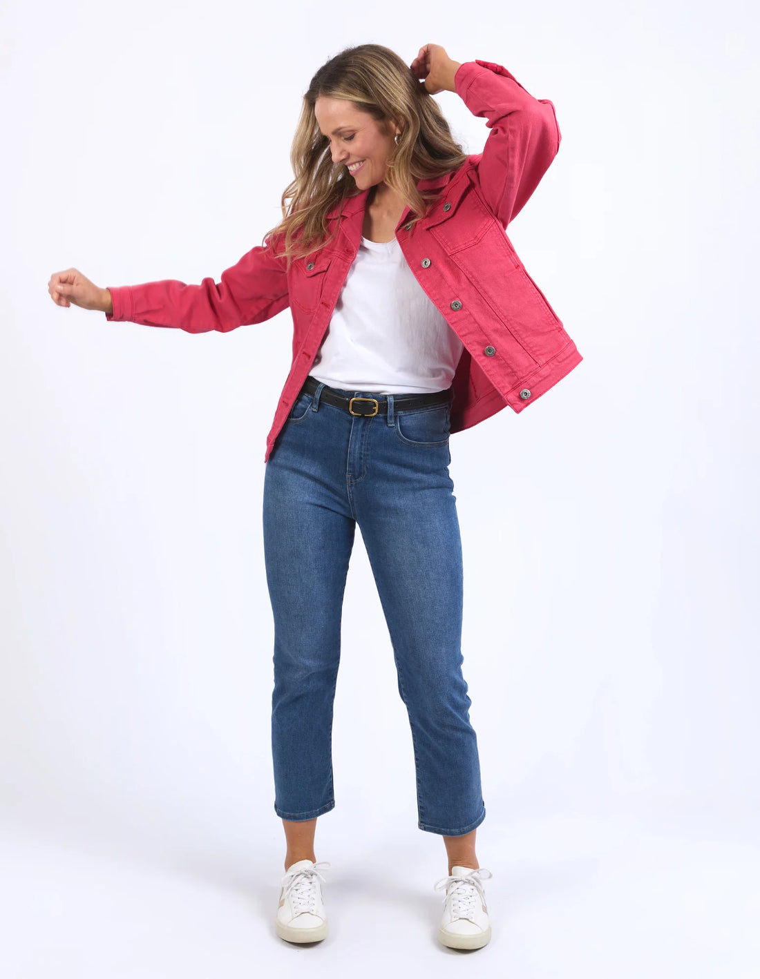 woman standing wearing white top with elm lifestyle tilly denim jacket in bittersweet red, denim pants with black belt, and white shoes