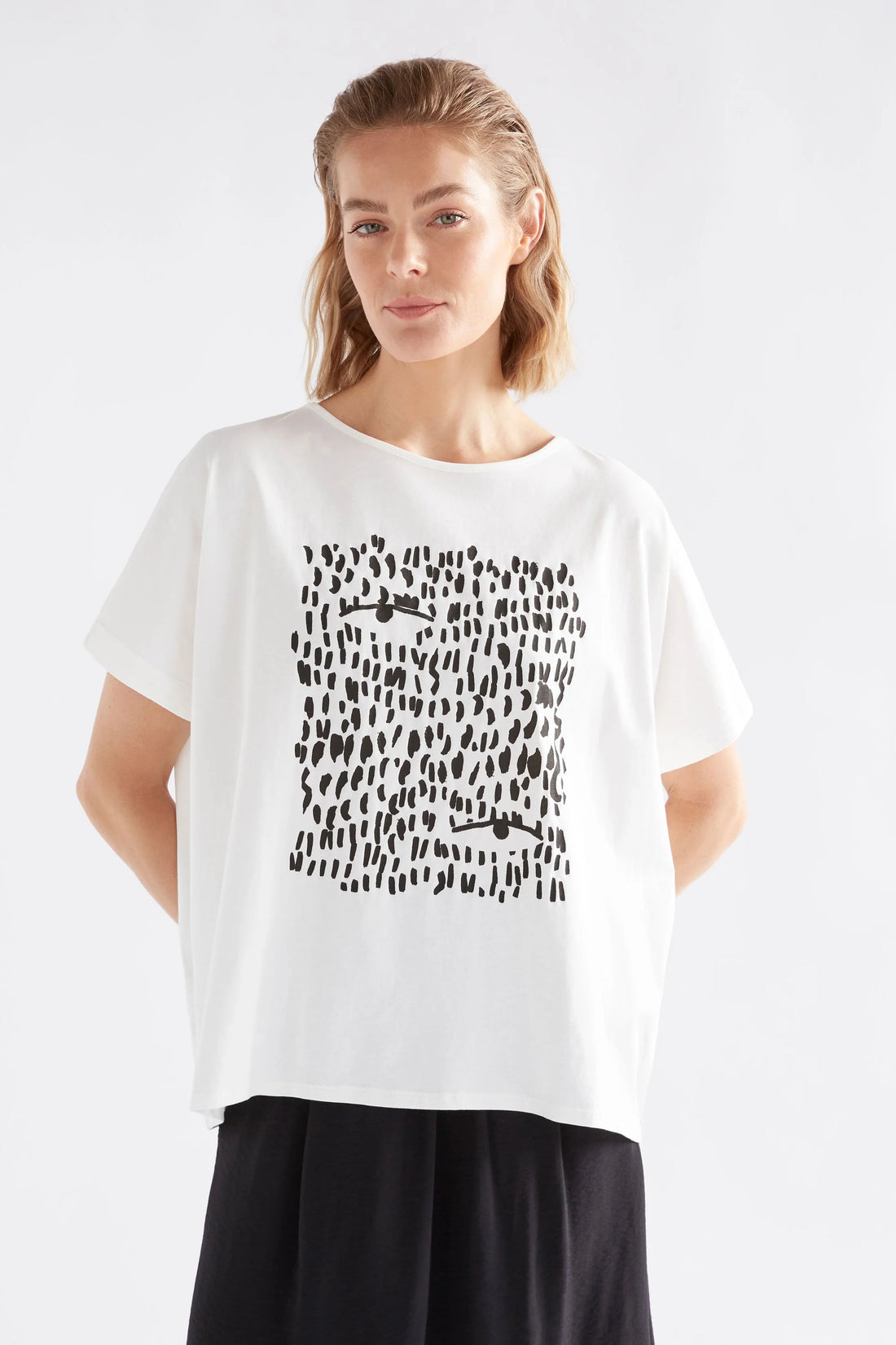 woman standing wearing black skirt and elk bruk tee with black tropea placement print