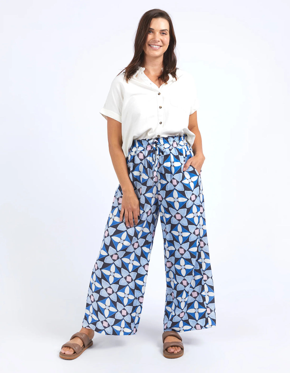woman wearing white top, elm lifestyle painted tile pant geo print, and brown slippers