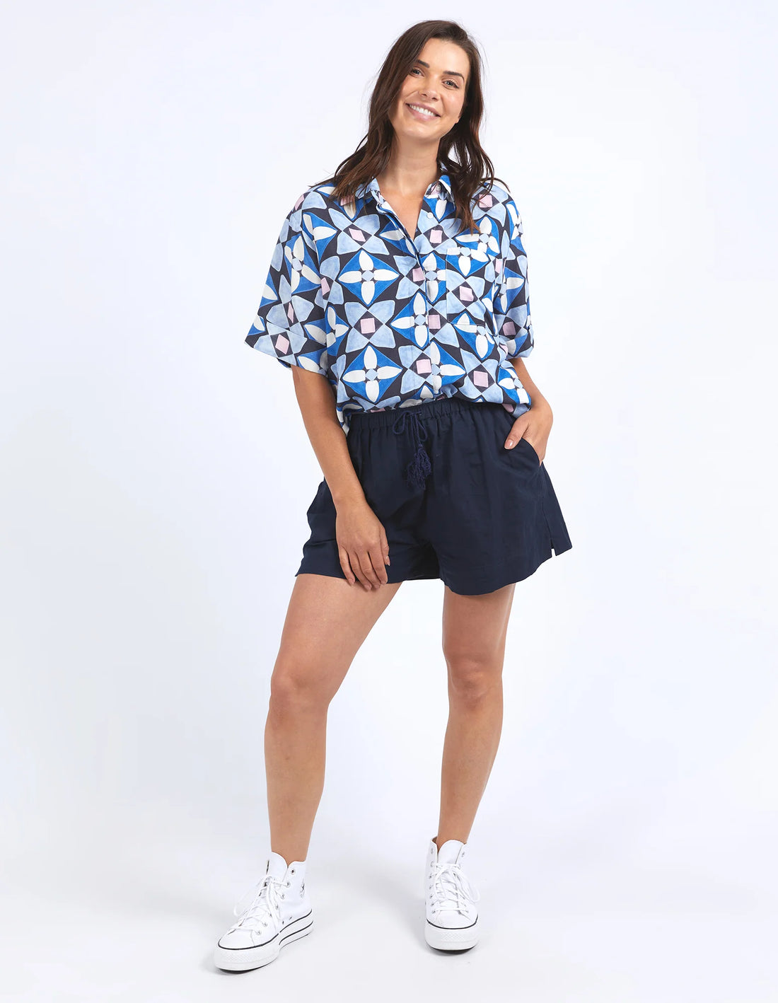 woman standing wearing elm lifestyle painted tile shirt geo print, drawstring short, and white converse shoes