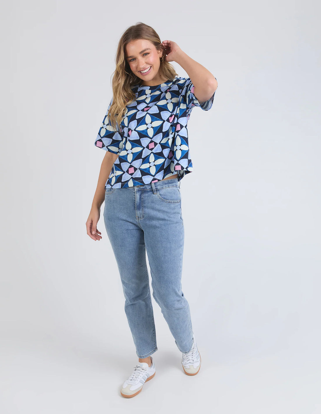 woman standing wearing elm lifestyle painted tile tee geo print, denim pants, and white shoes