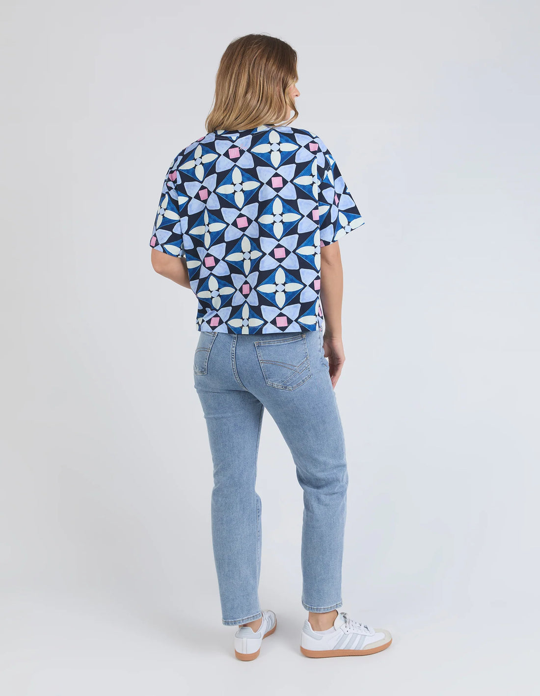 woman looking at the back wearing elm lifestyle painted tile tee geo print, denim pants, and white shoes