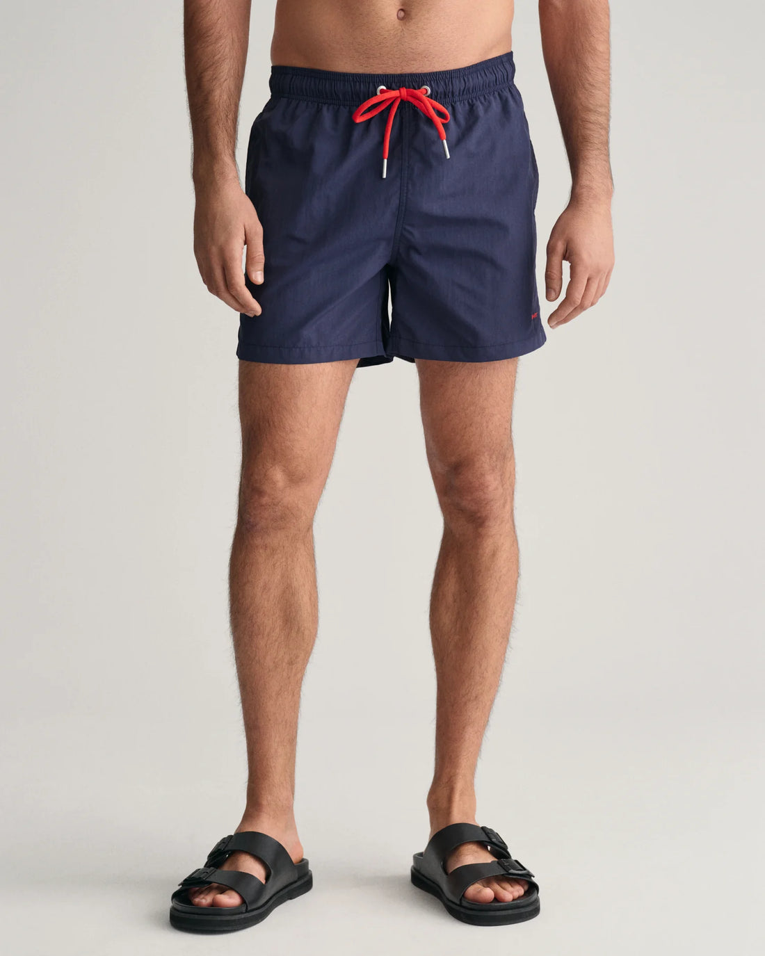 standing man wearing gant basic swim shorts in marine and black slip on