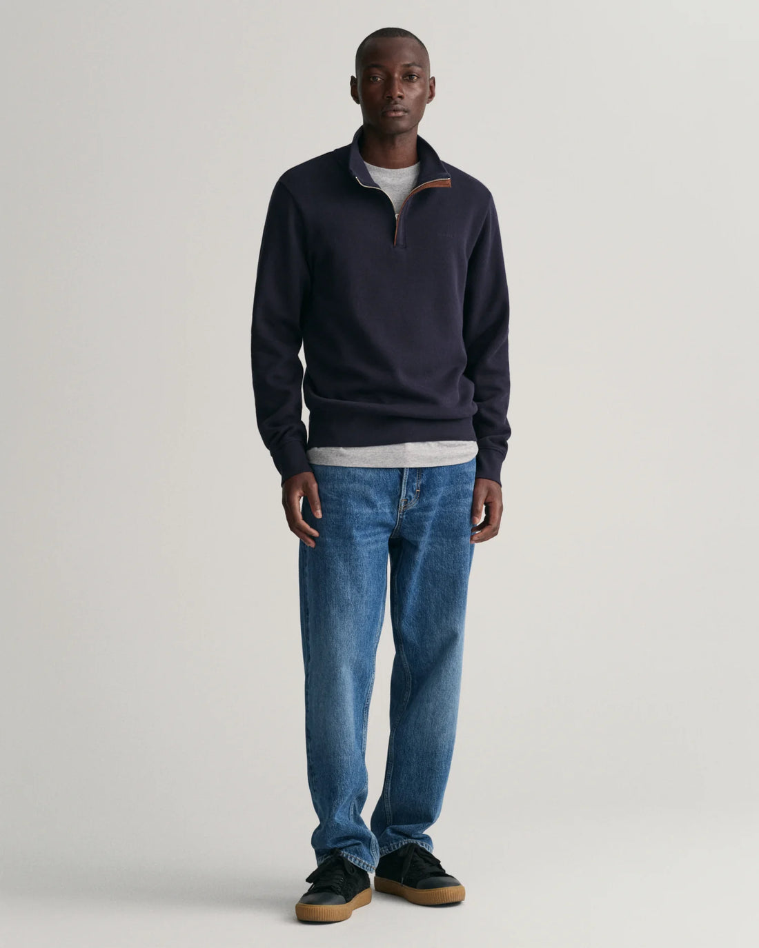 man wearing gant sacker rib half zip sweatshirt in evening blue, denim pants, black shoes