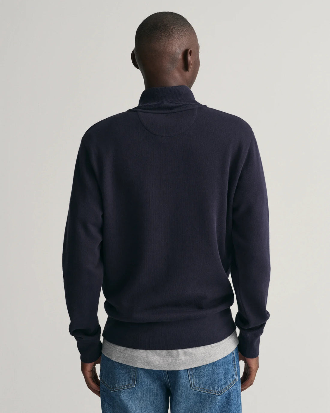 man facing the back wearing gant sacker rib half zip sweatshirt in evening blue, denim pants