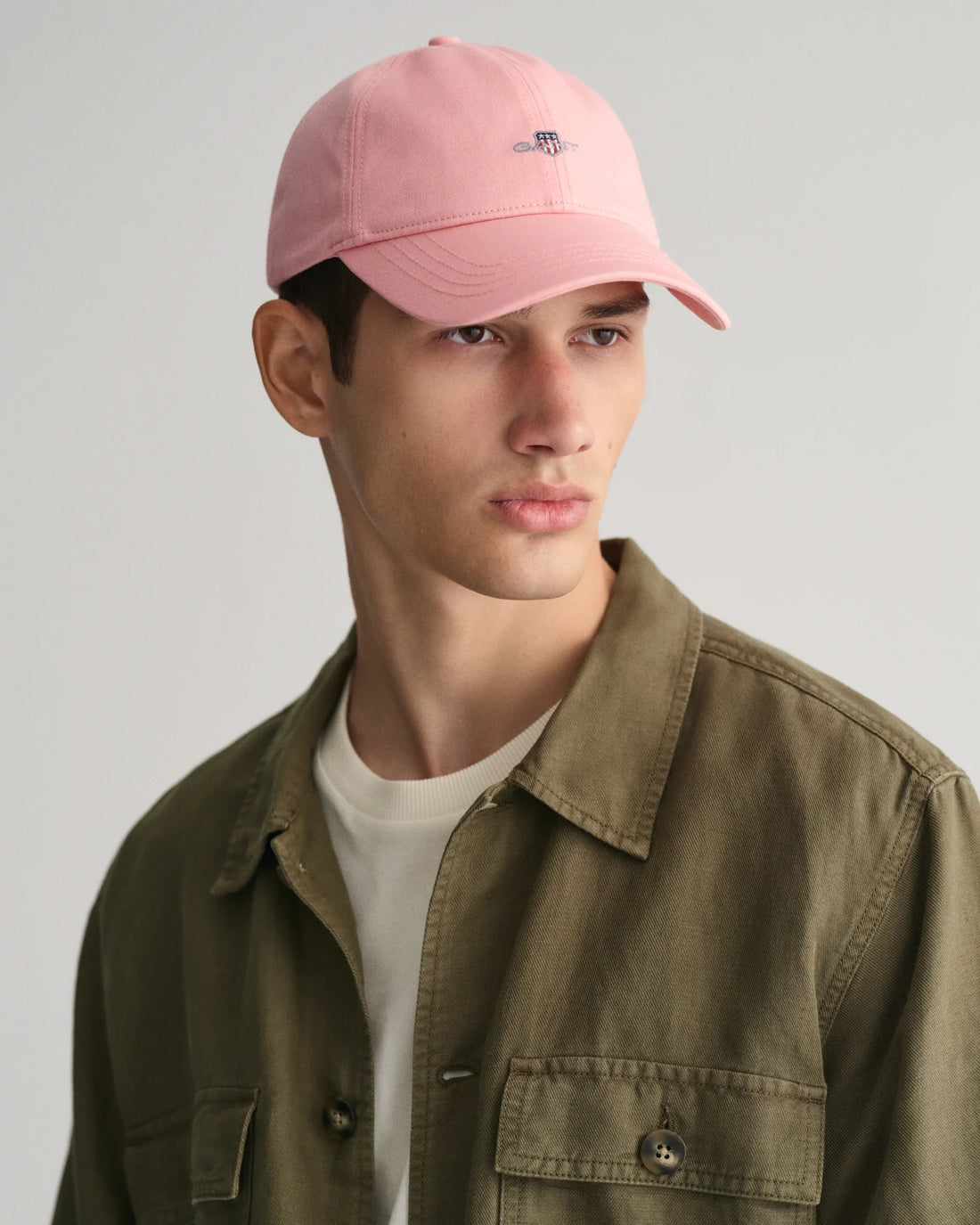 man wearing gant pink shield cap in pink, white shirt and khaki green short sleeve button down shirt