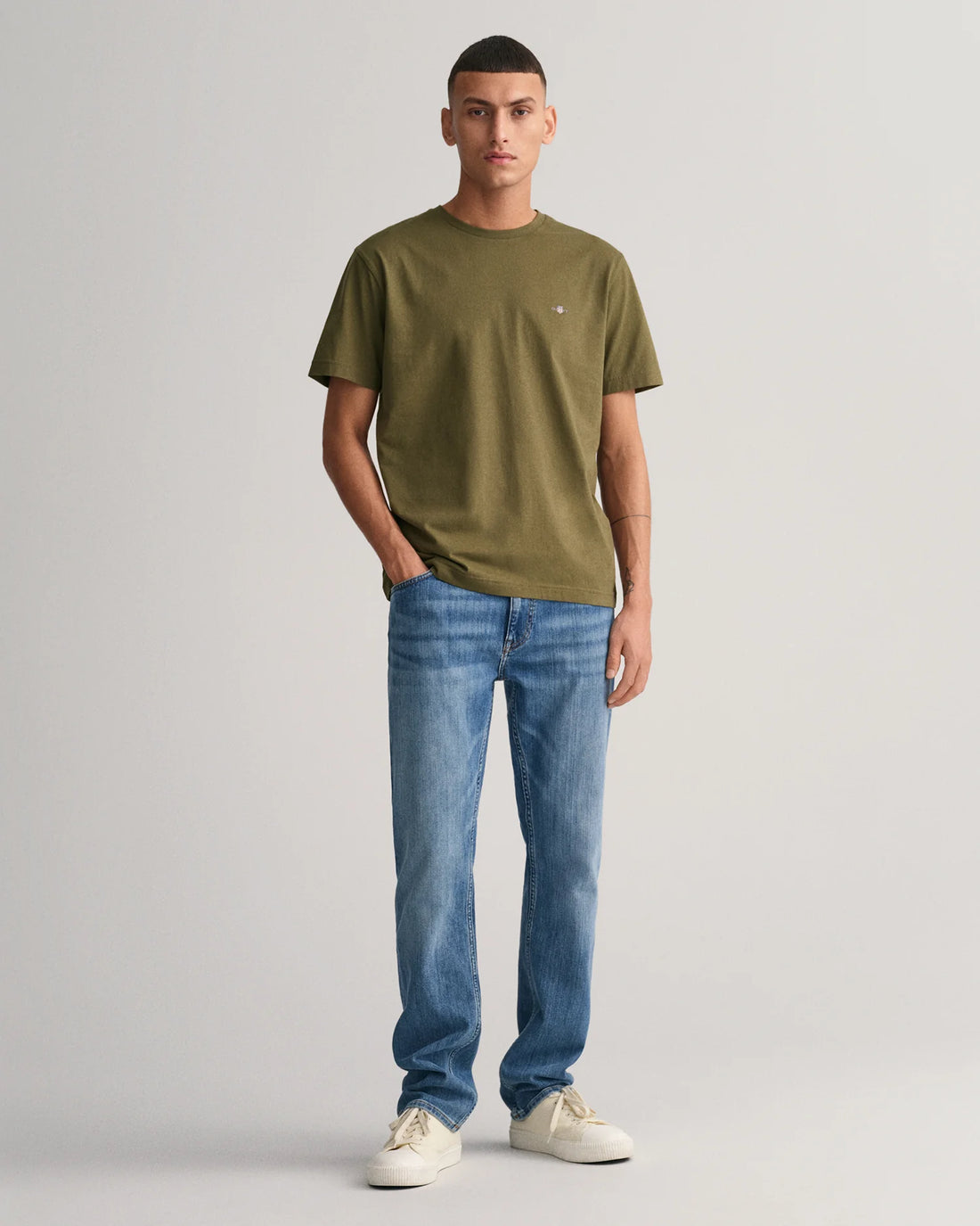 man standing wearing shield t-shirt in juniper green, denim pants and shoes