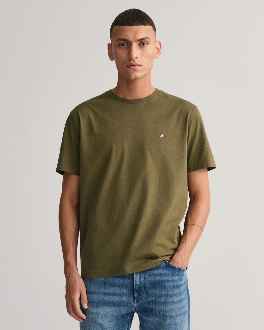 man standing wearing shield t-shirt in juniper green, denim pants