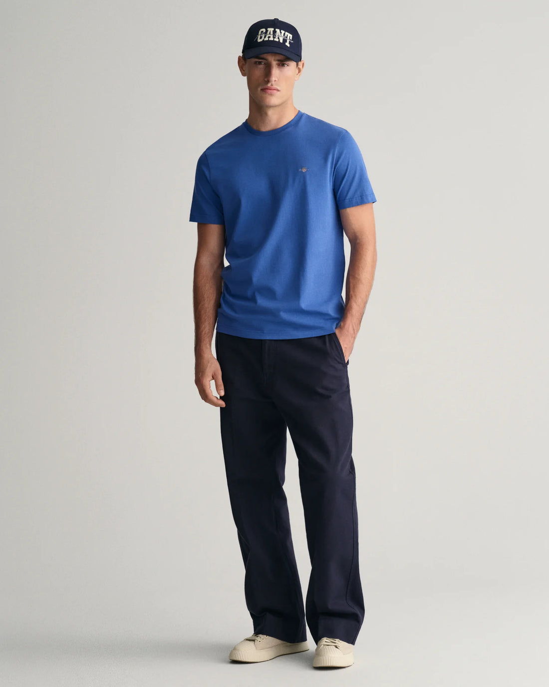 man standing wearing gant shield t-shirt in rich blue, navy blue pants and shoes