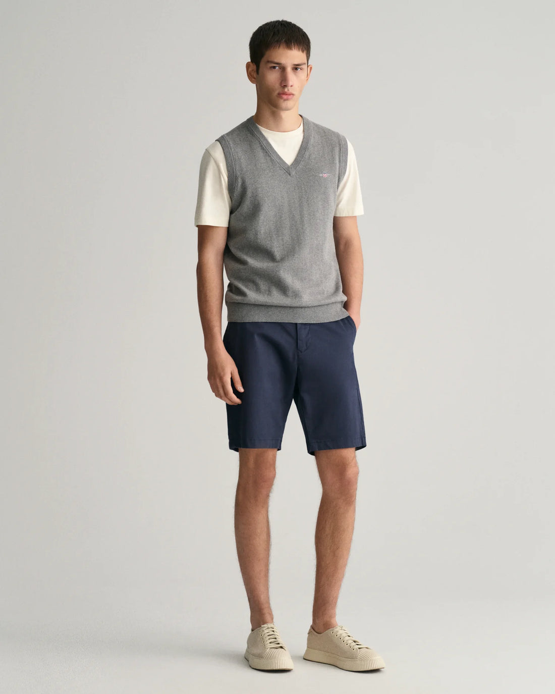 standing man wearing white top with grey vest, gant slim fit twill shorts in marine colour and rubber shoes