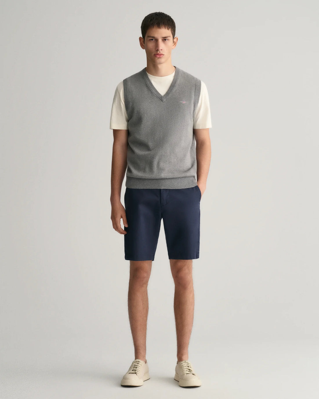 standing man wearing white top with grey vest, gant slim fit twill shorts in marine colour and rubber shoes