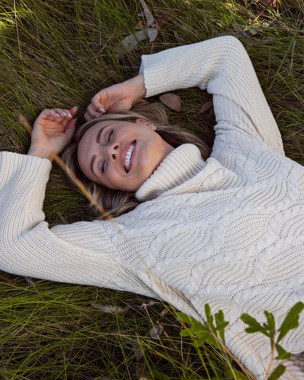 Woman wearing Wave Knit Sweater -Vanilla and dark denim pants lying on the grass