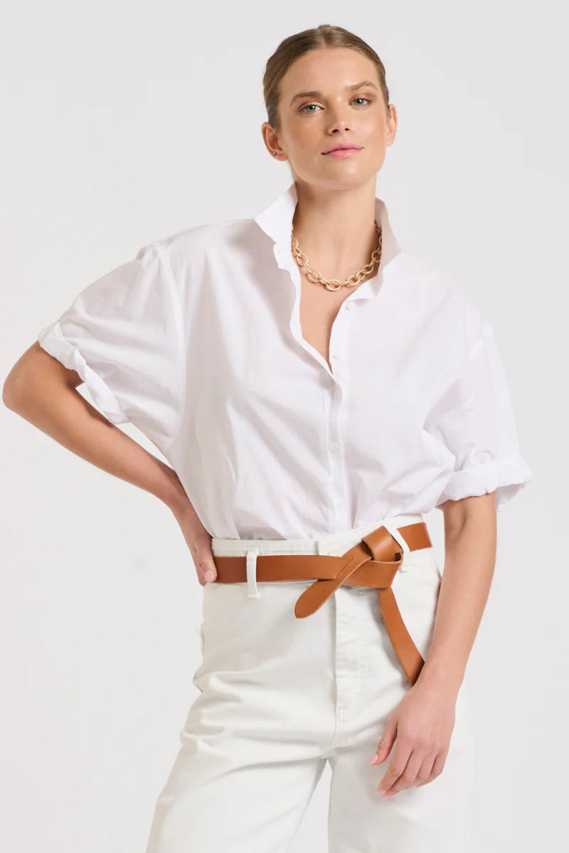 woman wearing white pants, brown belt, and tuck in shirty the annie relaxed short sleeve in white colour